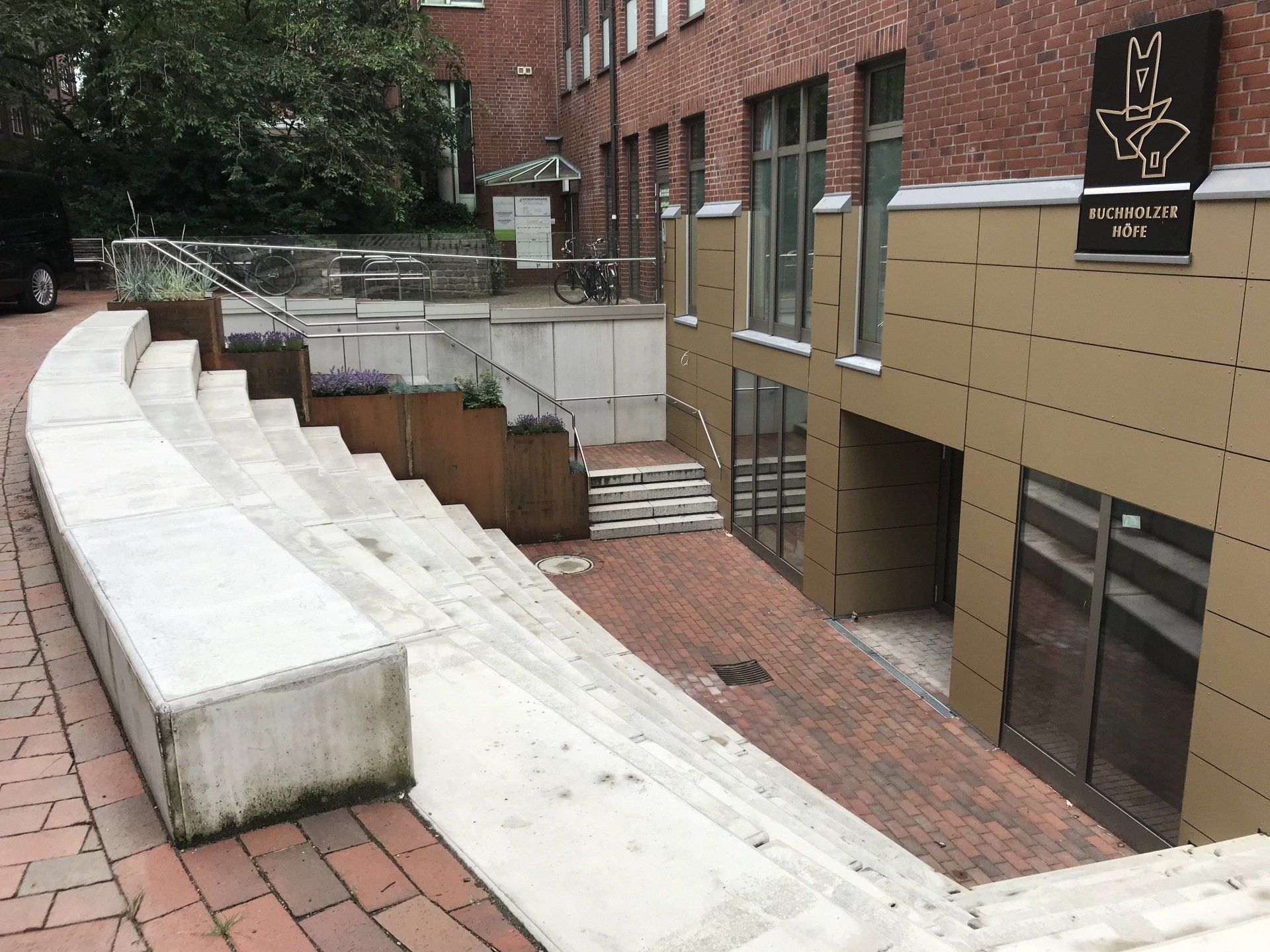 Außentreppe mit weißen Betonstufen neben einem Backsteingebäude und Eingängen im unteren Bereich.