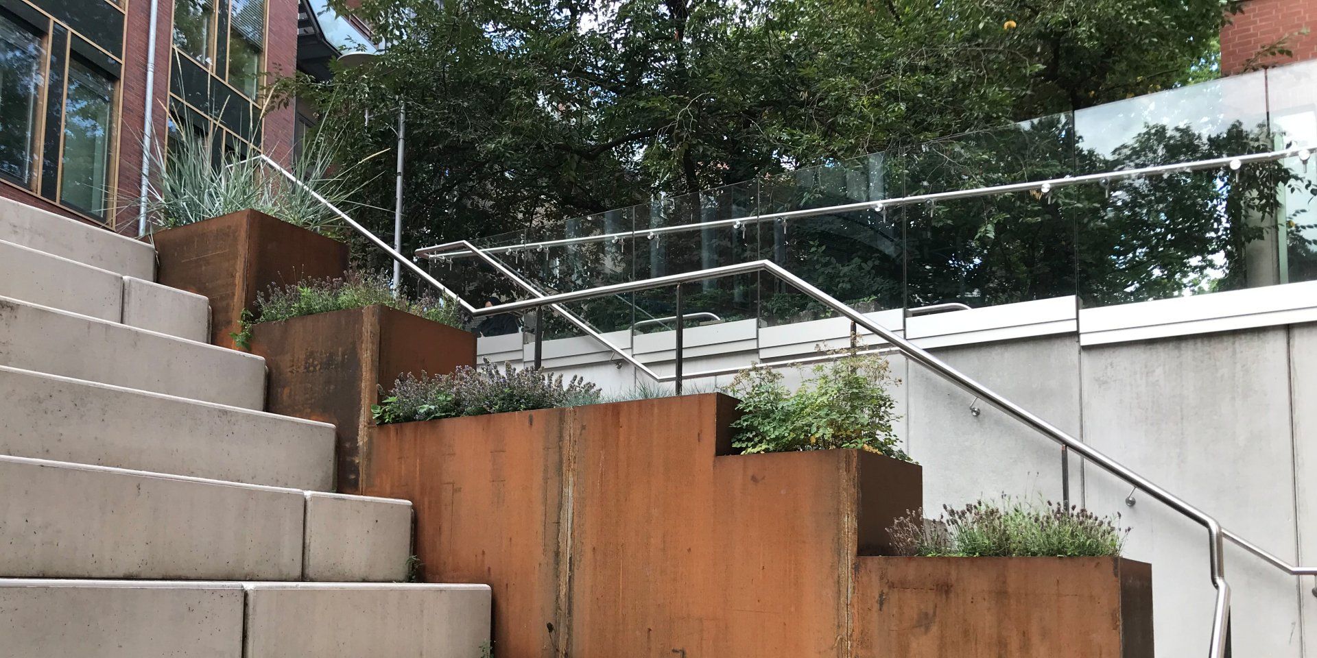 Moderne Außentreppe mit Betonstufen, Holzpflanzkästen und Metallgeländer neben Grünflächen