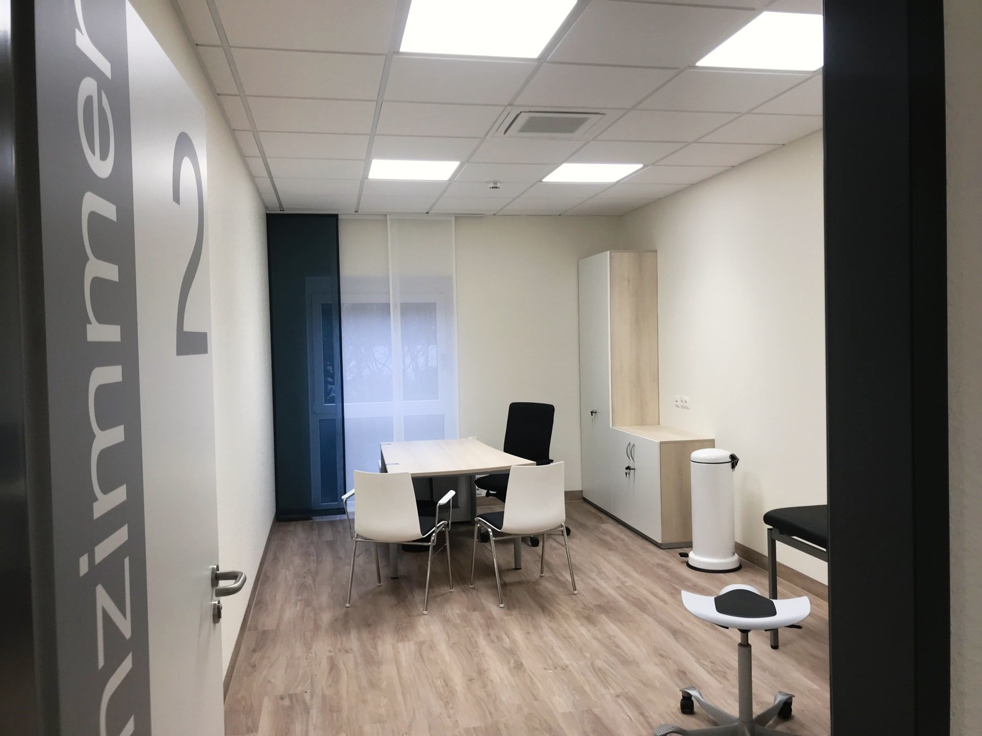 Leeres, modernes Büro mit weißem Tisch und Stühlen, Holzboden, Schränken und einem Fenster mit Jalousien.