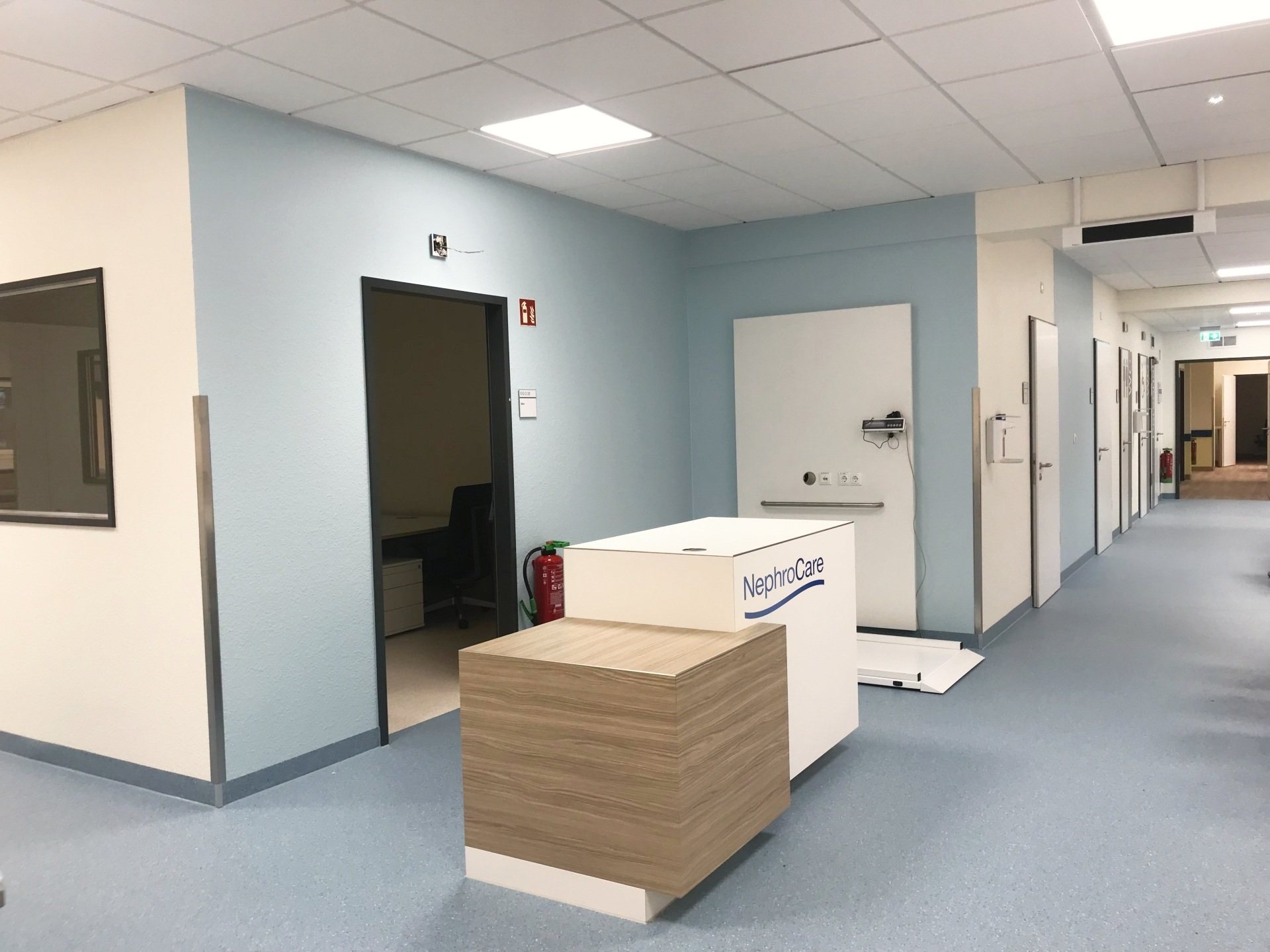 Leerer Büroflur mit blauen Wänden, offenen Türen und einem Stapel Kisten auf einem Wagen im Vordergrund