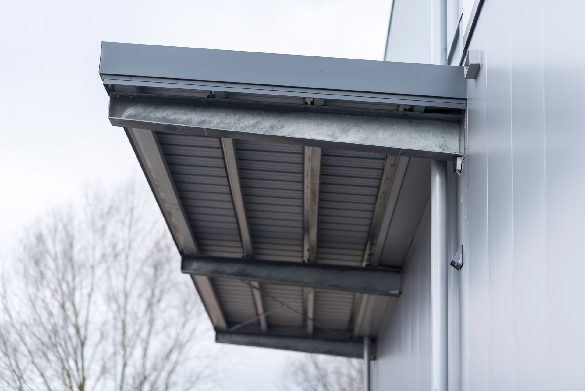 Graue Metallmarkise an der Außenfassade eines Gebäudes an einem bewölkten Tag