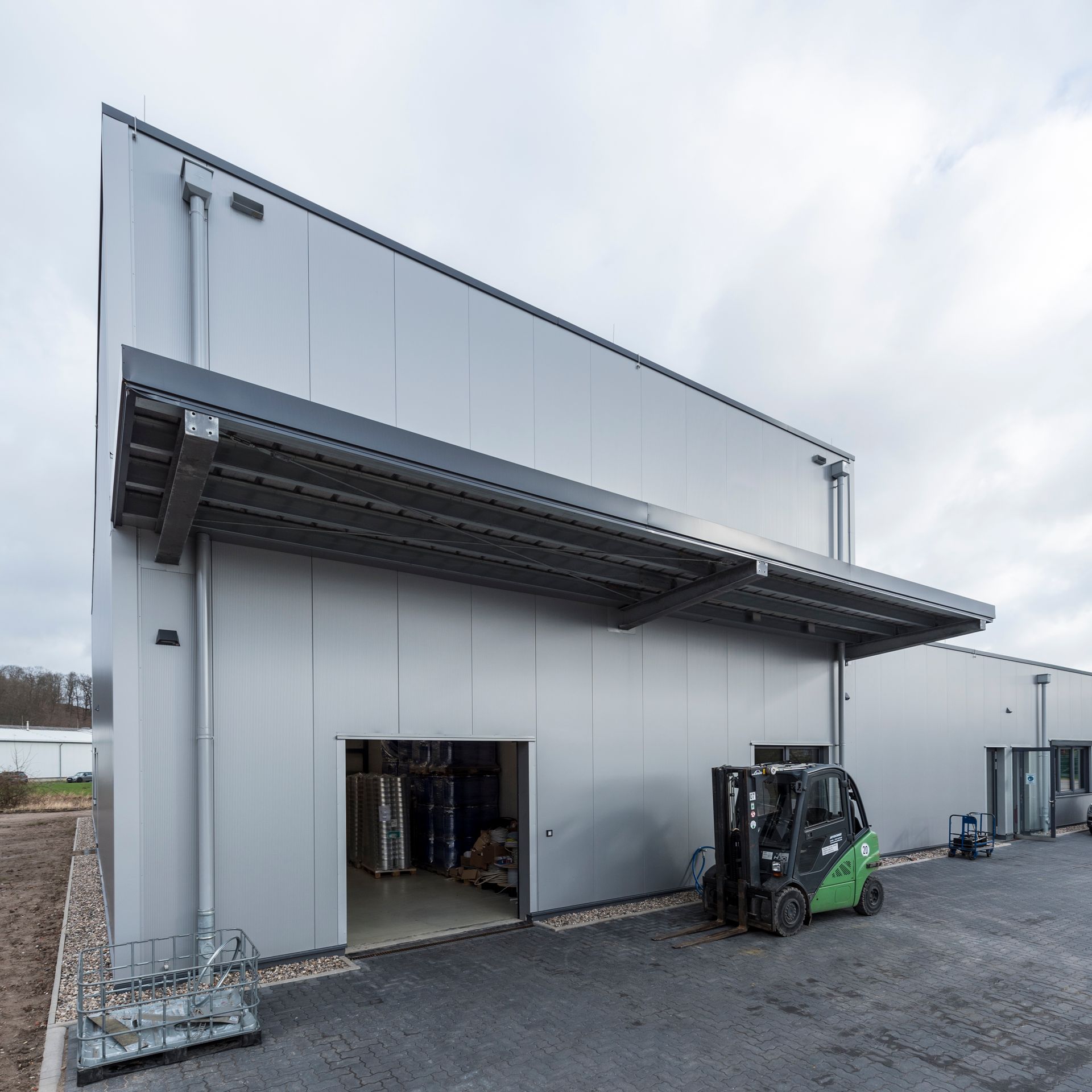 Außenansicht eines Industrielagers mit offener Laderampe und Gabelstapler auf einem Schotterplatz