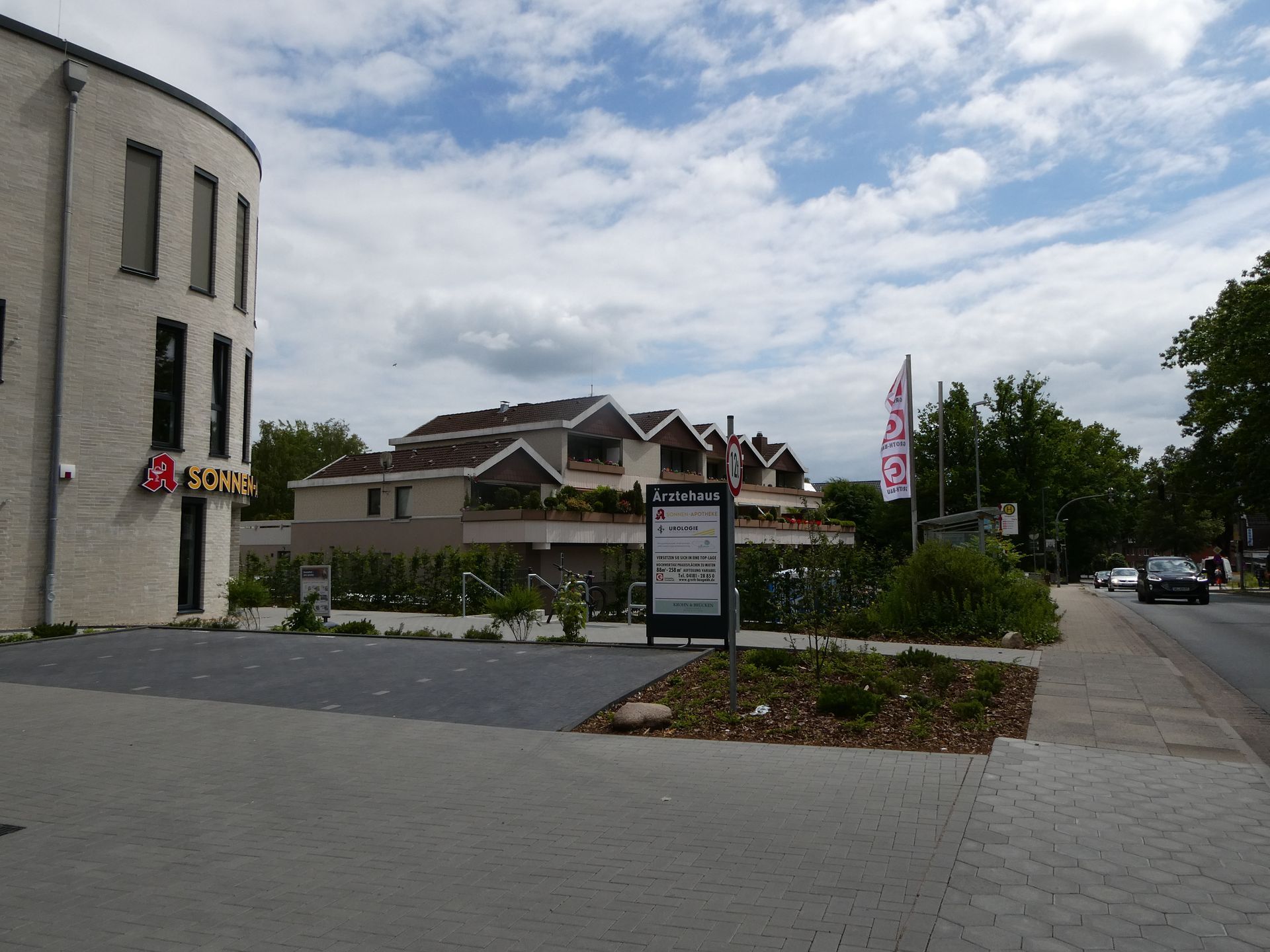 Eingang einer Wohnanlage mit Schild, angelegten Sträuchern und einer Auffahrt unter bewölktem Himmel