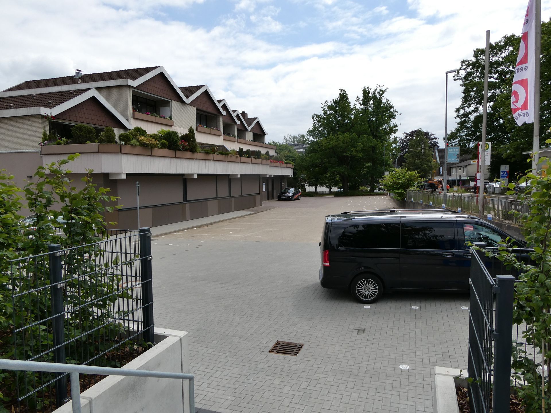  Innenhof mit geparktem schwarzen Lieferwagen, niedrigen Gebäuden und Bäumen unter einem bewölkten Himmel