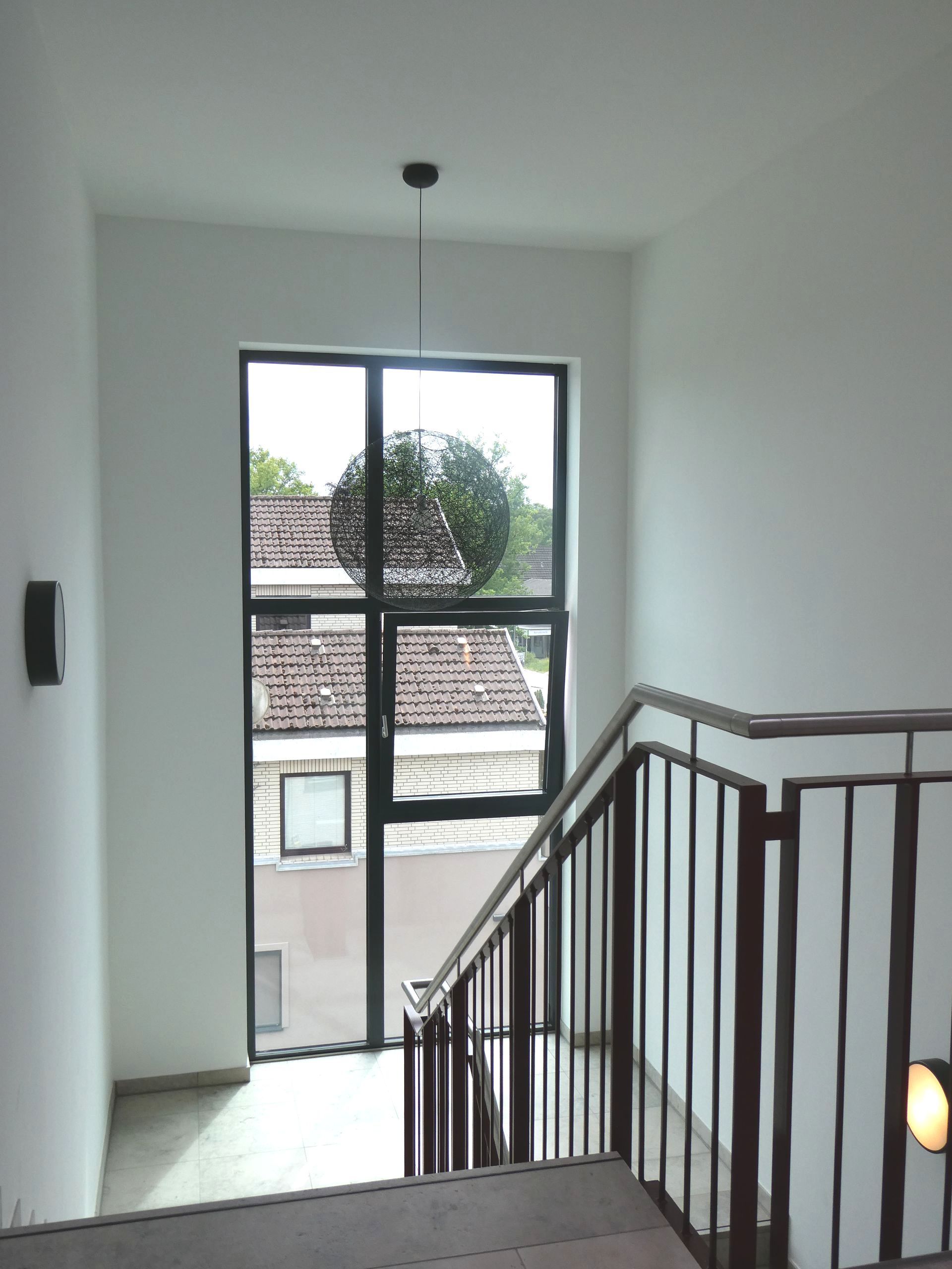 Treppenabsatz mit Fenster, weißen Wänden und Metallgeländer mit Blick auf die Dächer draußen