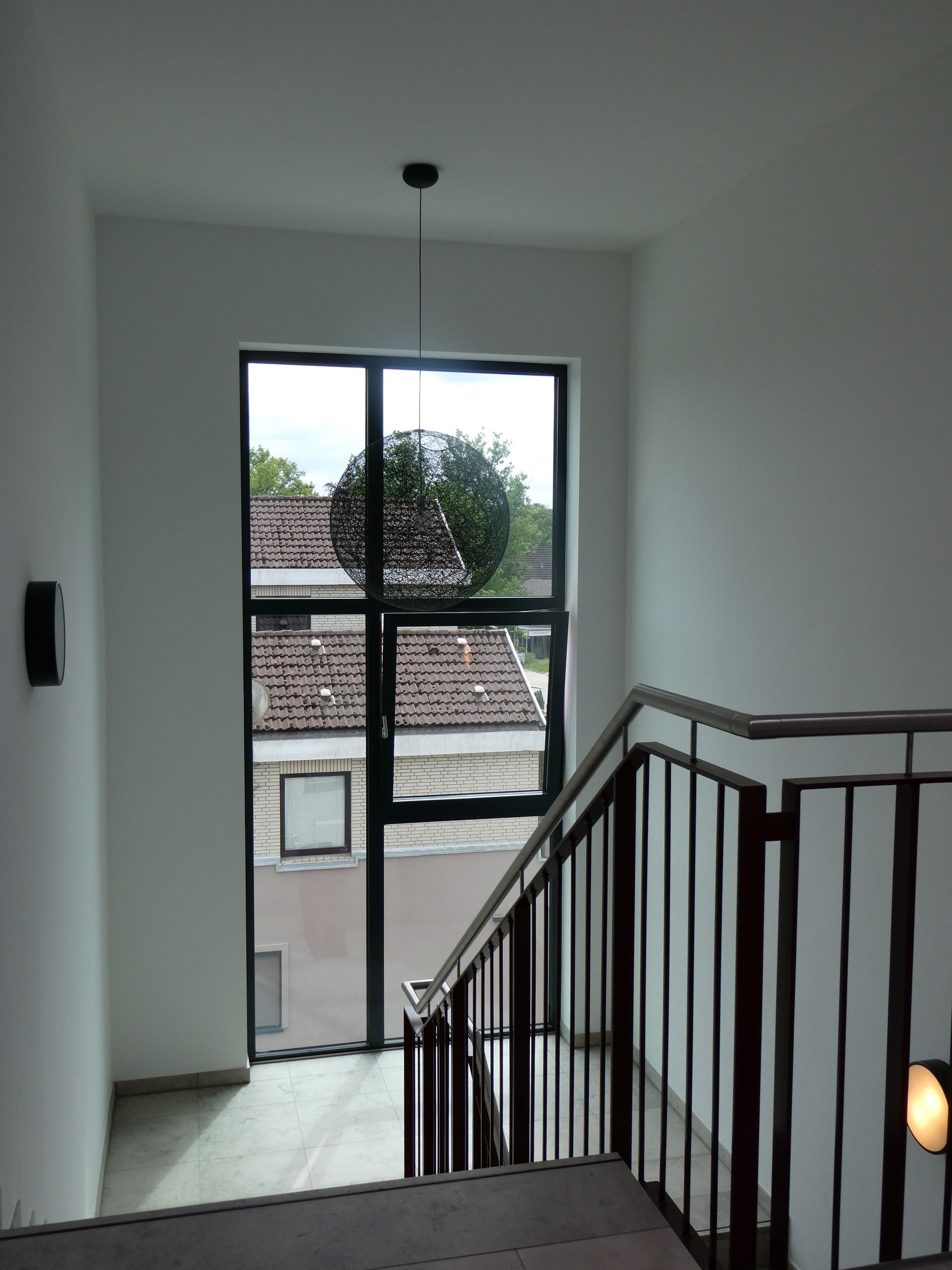 Heller Treppenabsatz mit schwarzem Geländer und einem Fenster mit Blick über die Dächer.