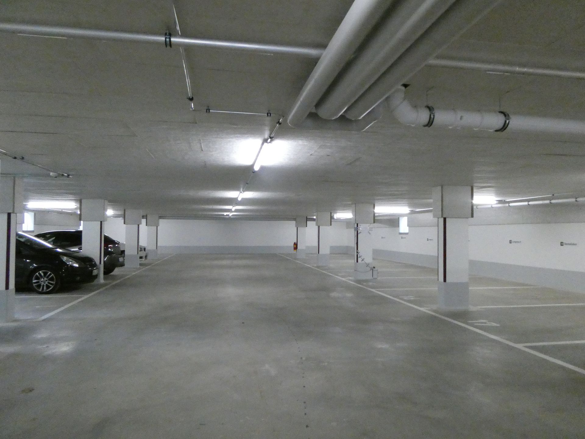Leere Tiefgarage mit Betonpfeilern und geparkten Autos auf der linken Seite.