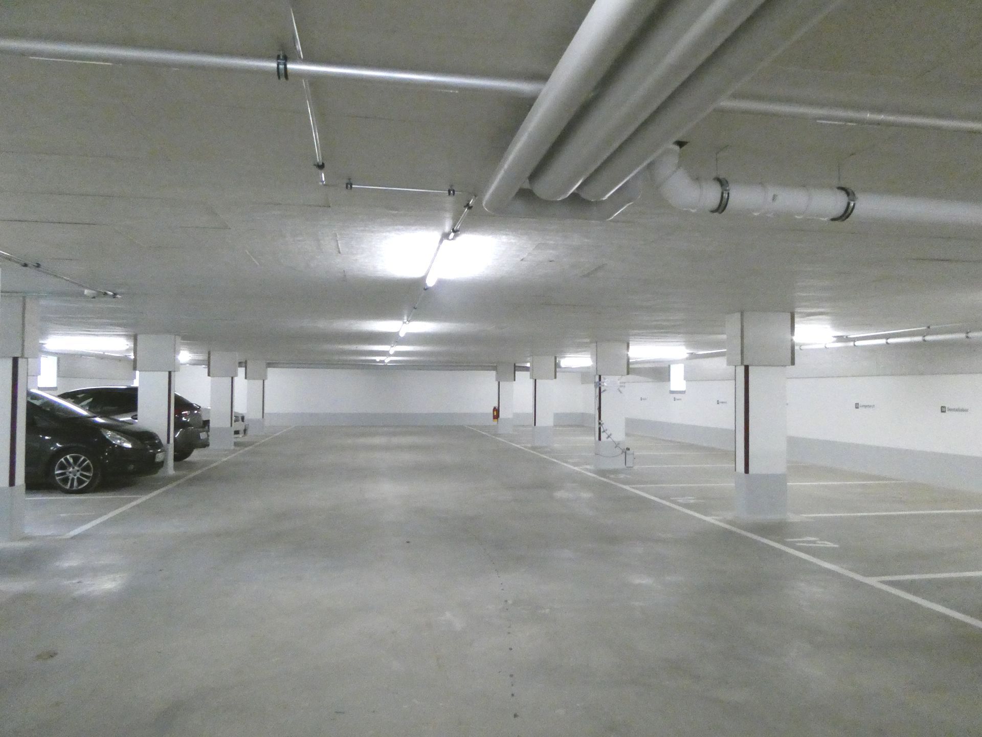 Leere Parkgarage aus Beton mit Neonröhren und ein paar geparkten Autos.