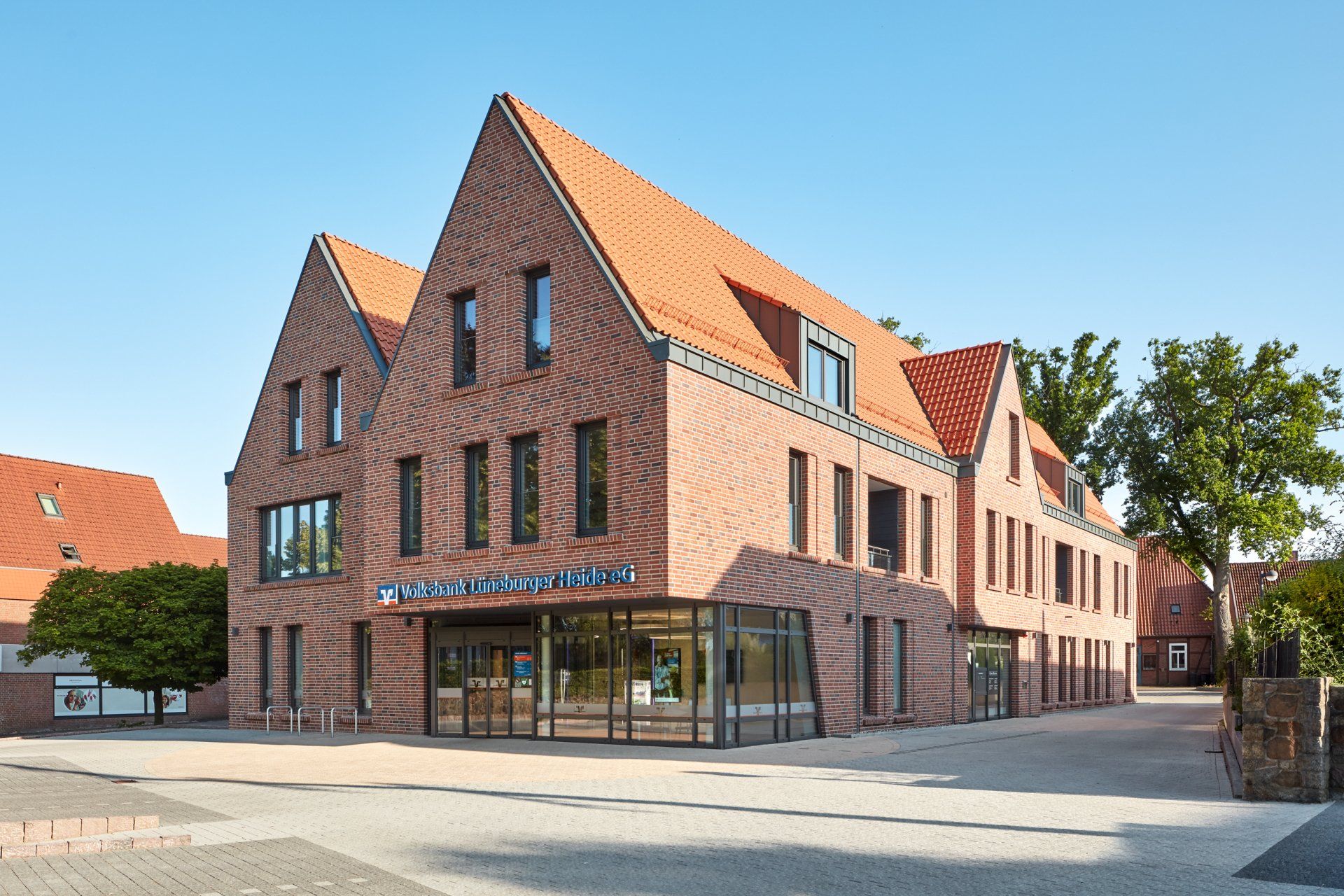Backsteingebäude mit steilen roten Dächern und Schaufenstern an einer sonnigen Straßenecke