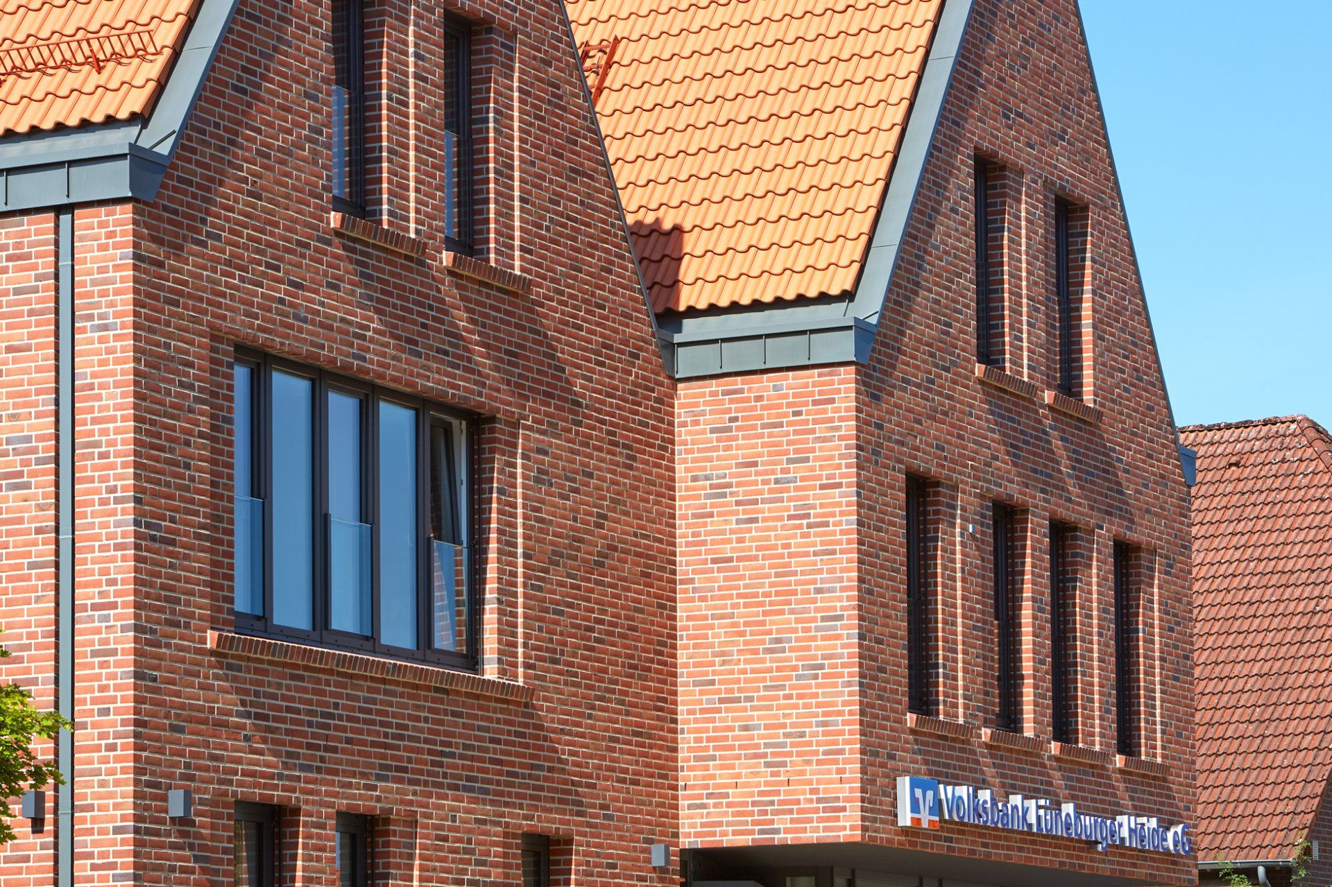 Backsteingebäude mit orangefarbenen Dachziegeln und blau umrandeten Fenstern unter klarem Himmel