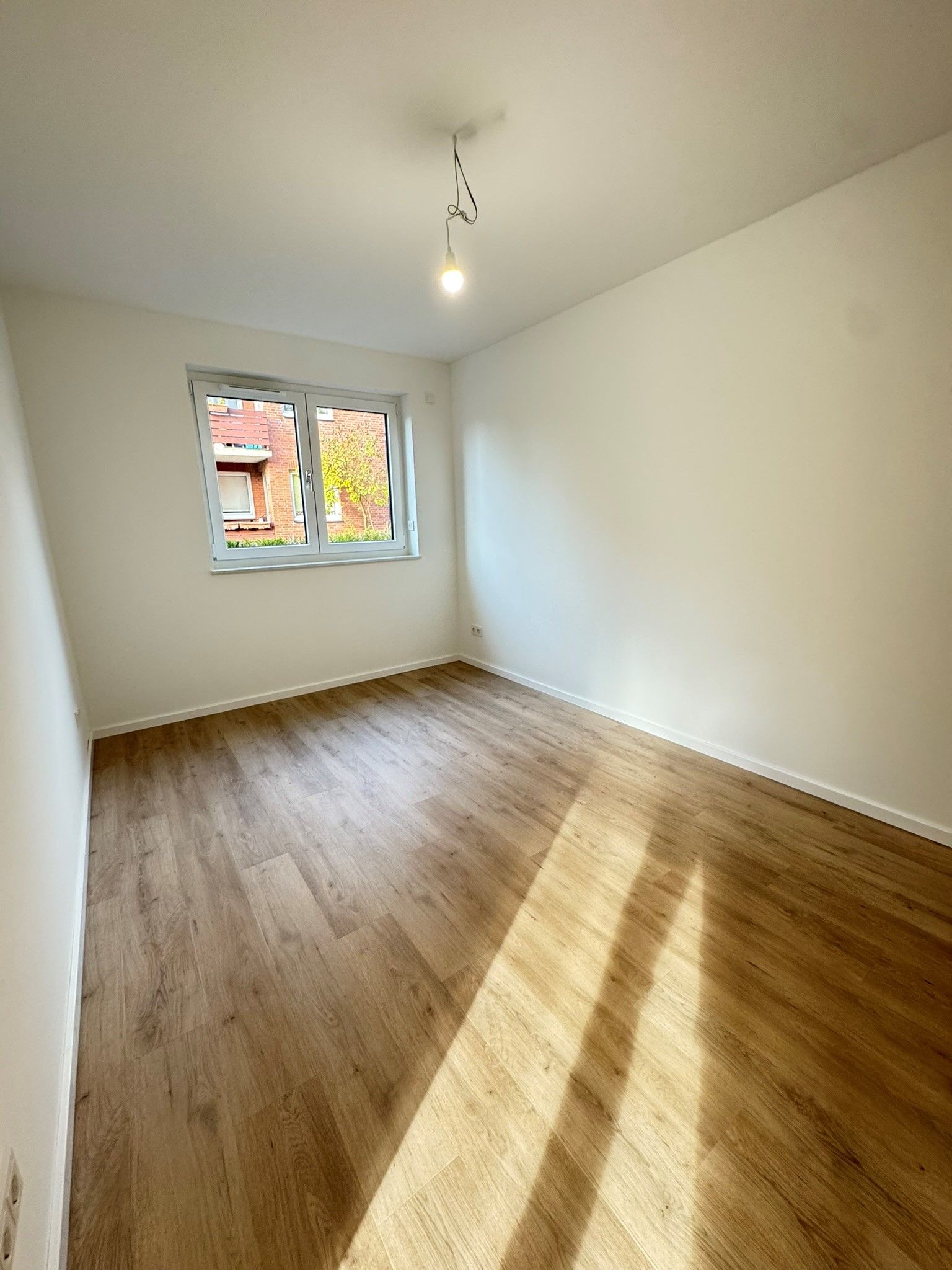 Leerer weißer Raum mit Holzboden, Fenster und von links einfallendem Sonnenlicht