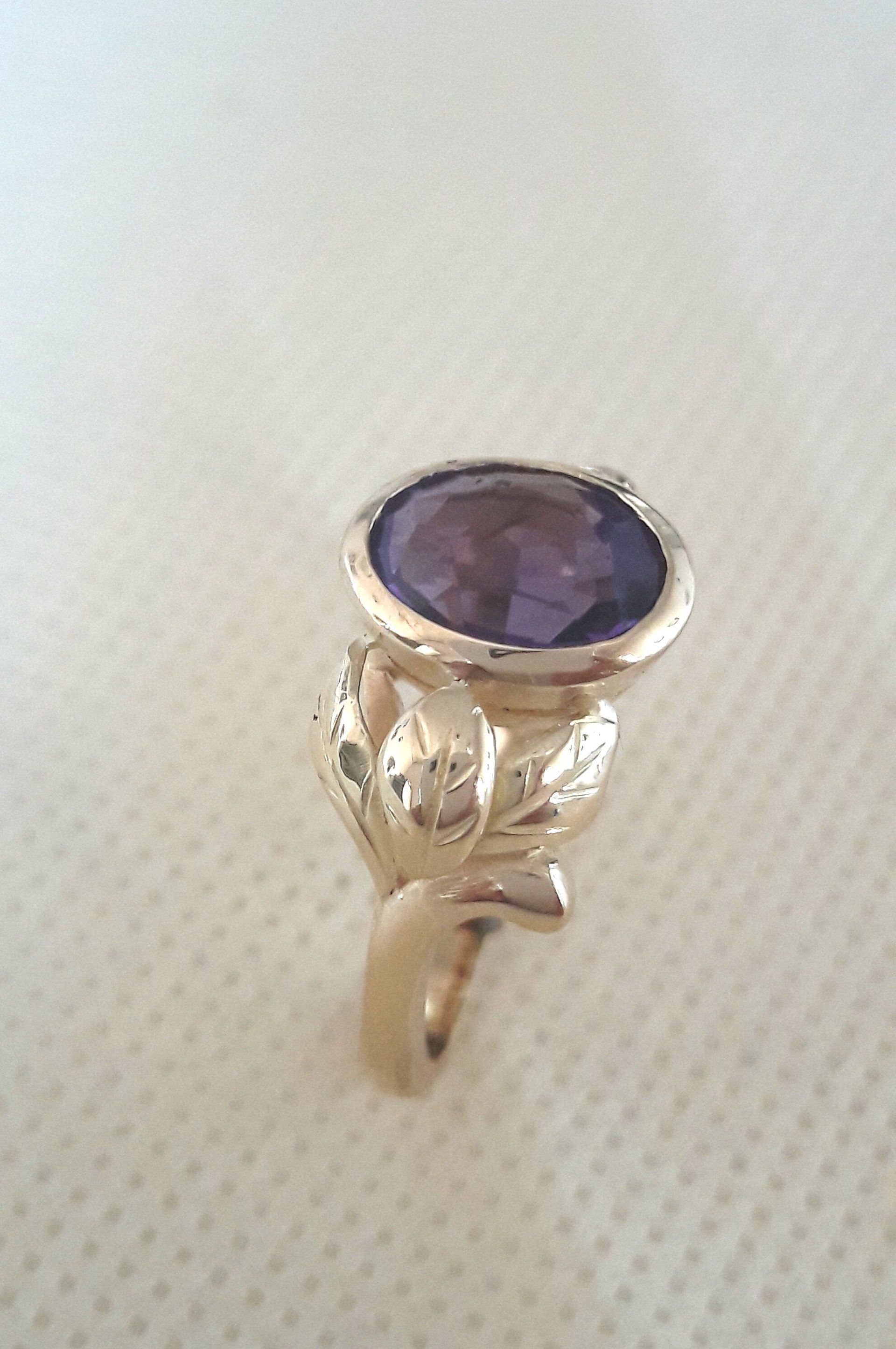 Gold ring with an oval, purple gemstone and ornate leaf details.