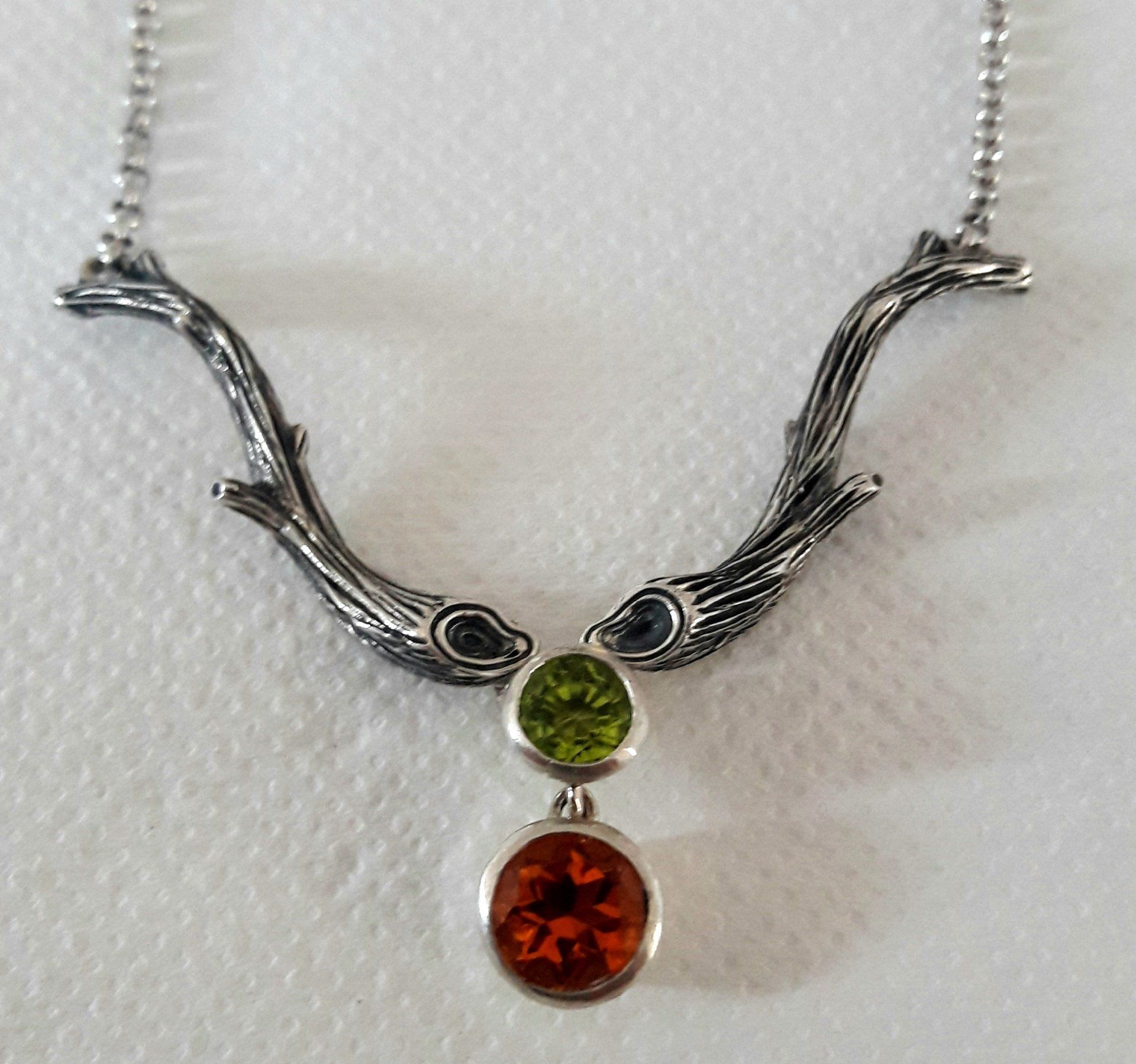 Silver twig necklace with green and orange gemstones.