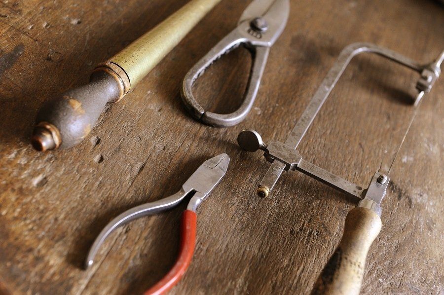 Assortment of metalworking tools: pliers, shears, file, and saw on a wooden surface.