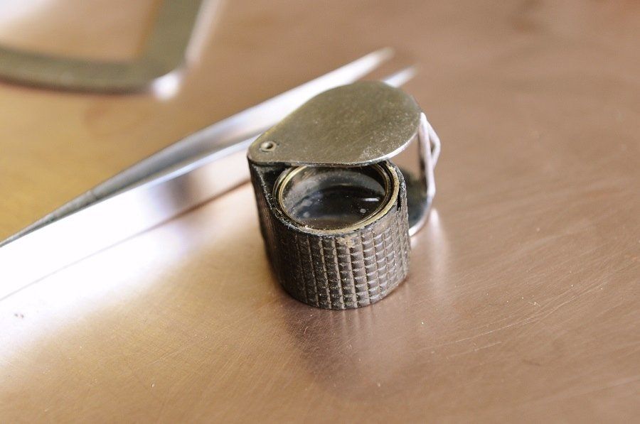Foldable magnifying glass and tweezers on a copper-colored surface.