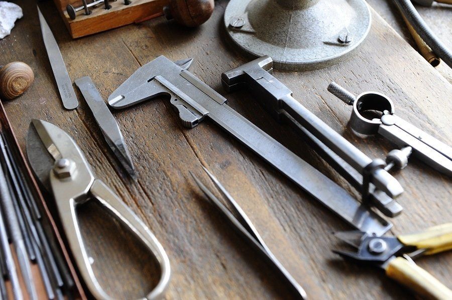 Jeweler's tools: calipers, pliers, files, and other metalworking instruments on a wooden surface.
