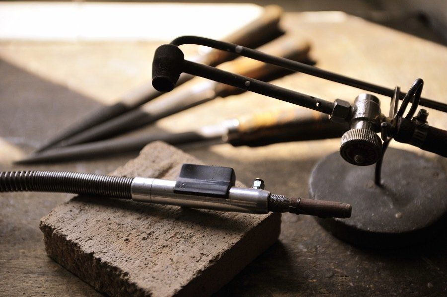 Jeweler's tools: torch on brick, metal files in background.