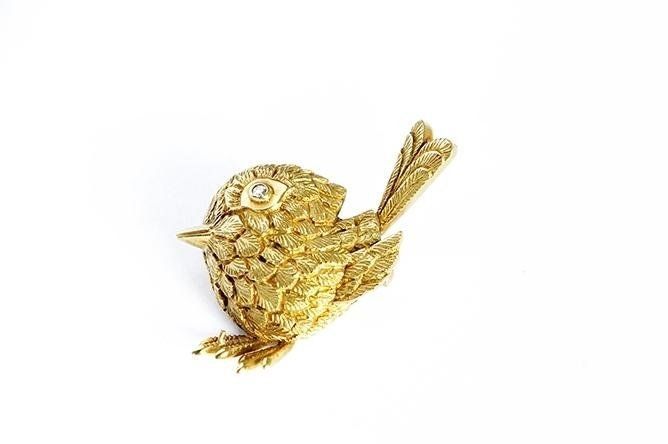 Gold-colored bird brooch with textured feathers and two small gems for eyes.