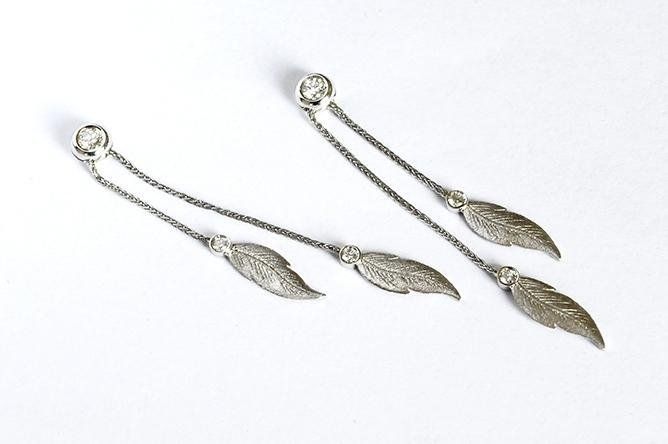 Silver feather drop earrings on a white background.