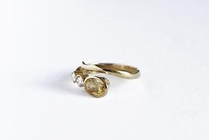 Gold ring with a large yellow gem, small diamonds, and a curved band on a white surface.