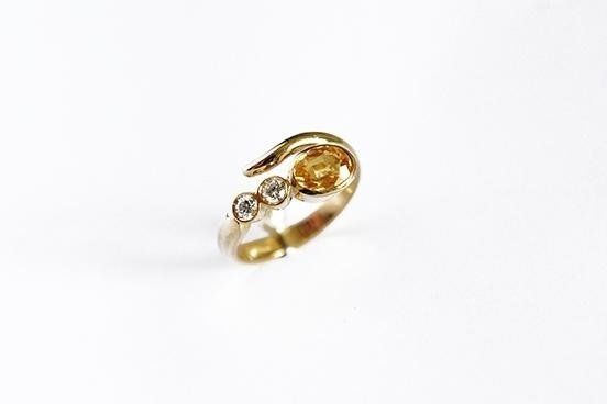 Gold ring with a yellow gemstone and two small clear stones, on a white surface.