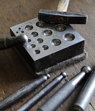 Metalworking tools: a dapping block, hammers, and ball-ended punches on a wooden surface.