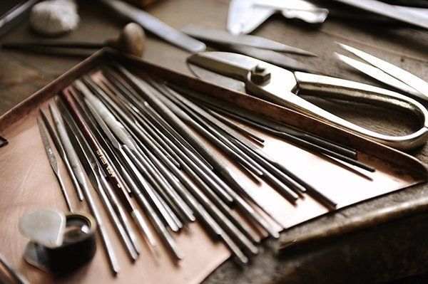 Close-up of a workshop table with various metalworking tools and materials, including files, shears, and copper sheets.