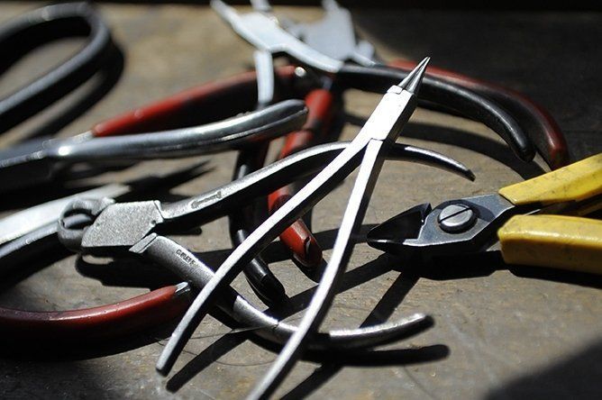 Close-up of various metal pliers with red and yellow handles, lying on a surface.