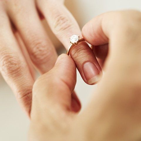 A hand putting a gold ring with a diamond on another hand's finger.