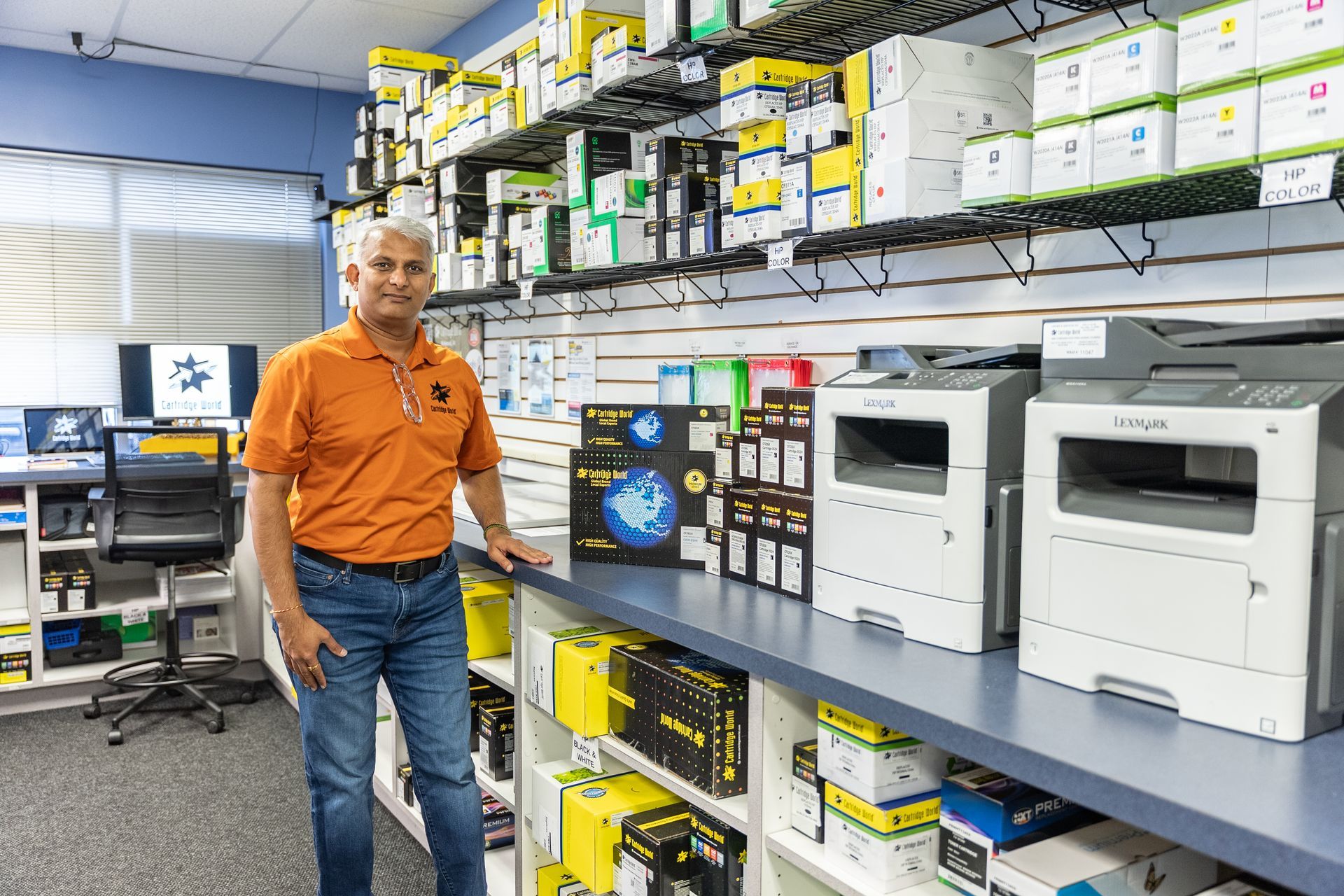 Office supply store interior: Printers and supplies on shelving. Signage on the walls.