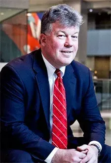 Man in a suit and red tie, smiling indoors.