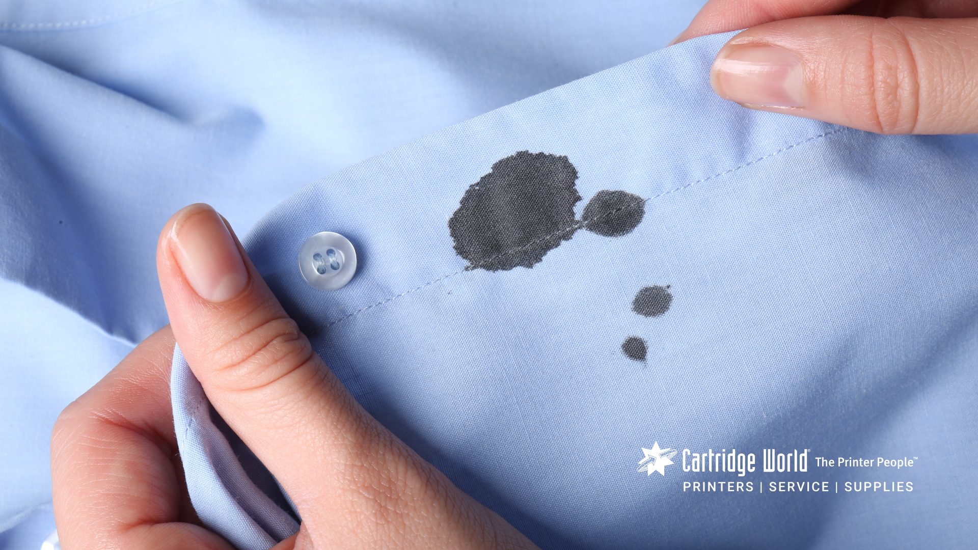 Hands holding a light blue shirt with dark stains near the button.