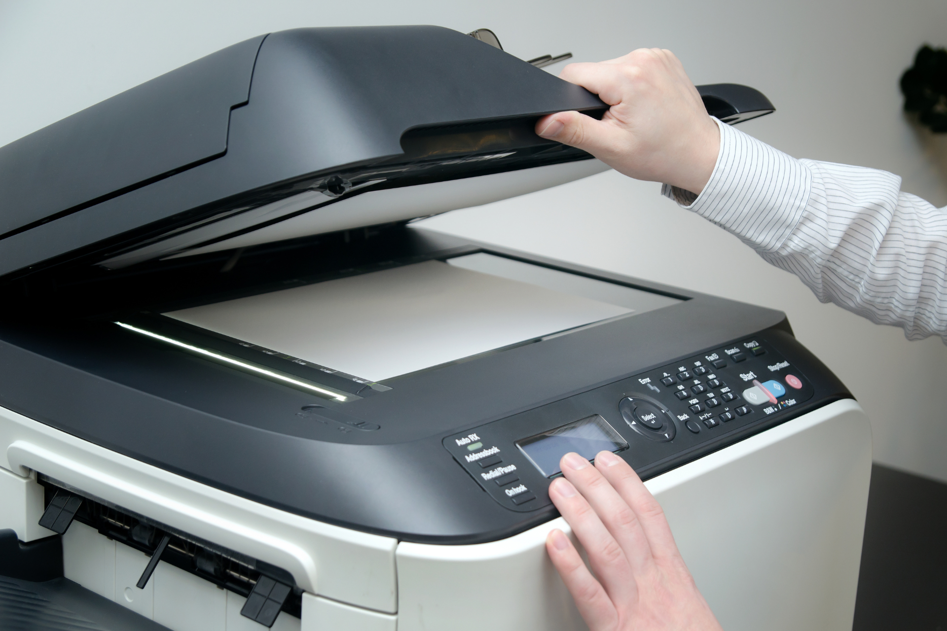 Person opening the lid of a multifunction printer, preparing to scan.