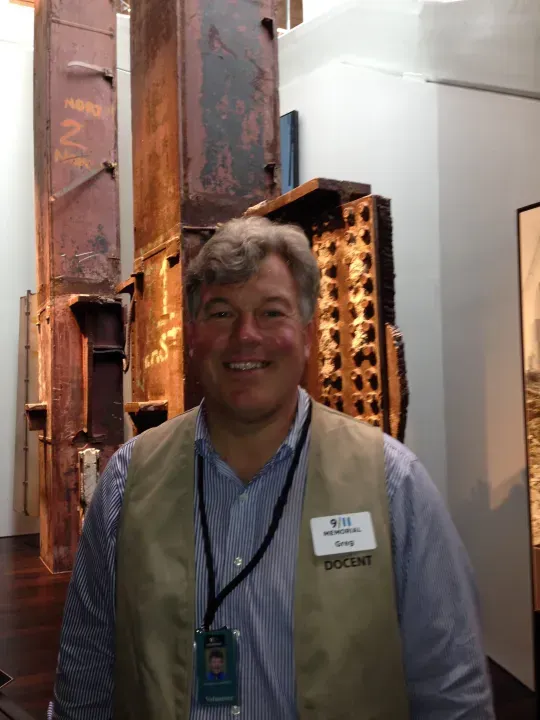 Man wearing a vest, smiling, in front of a 9/11 exhibit steel structure.