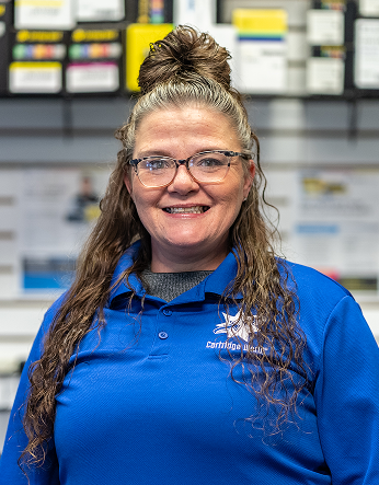 Woman wearing glasses in a blue polo shirt smiles, with hair pulled up.