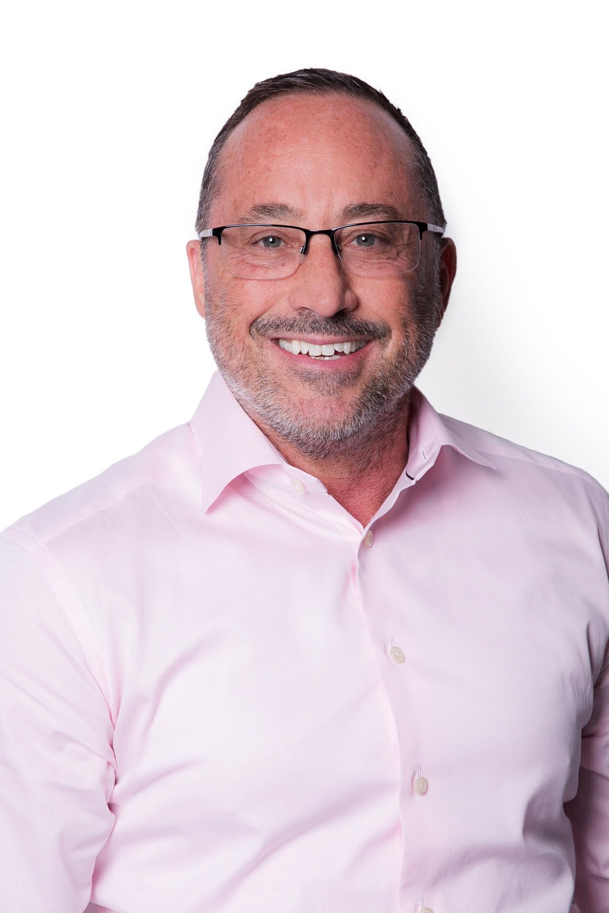 Man with glasses, light pink shirt smiles at the camera against a white background.