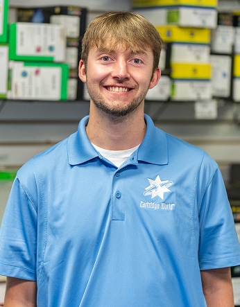 Man wearing a blue polo shirt smiles in a store, products on shelves in the background.