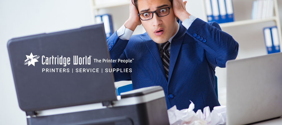 A man in a suit looks shocked with hands on his head, staring at a jammed printer.