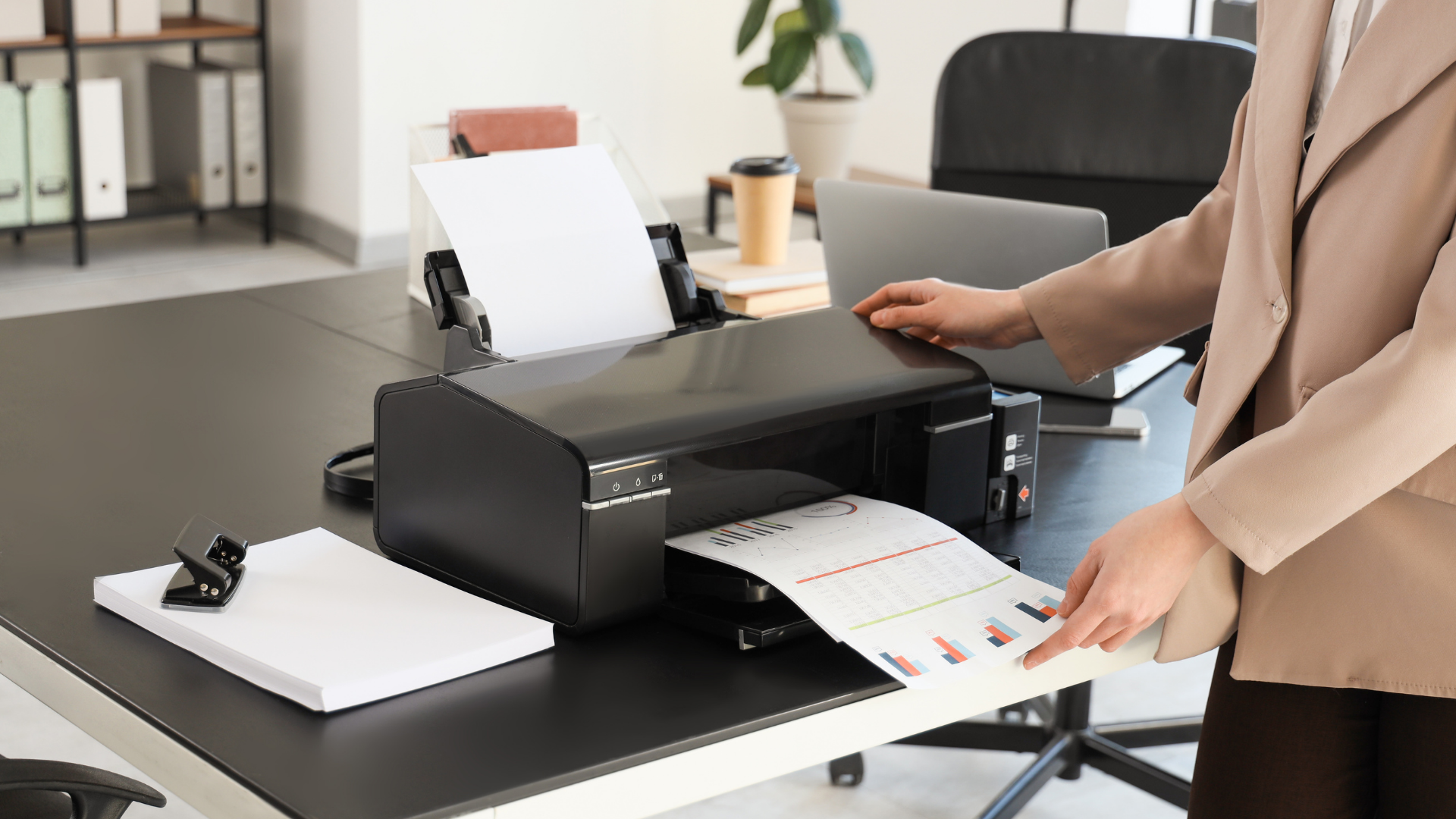 Person printing a document from a black printer on a desk in an office.
