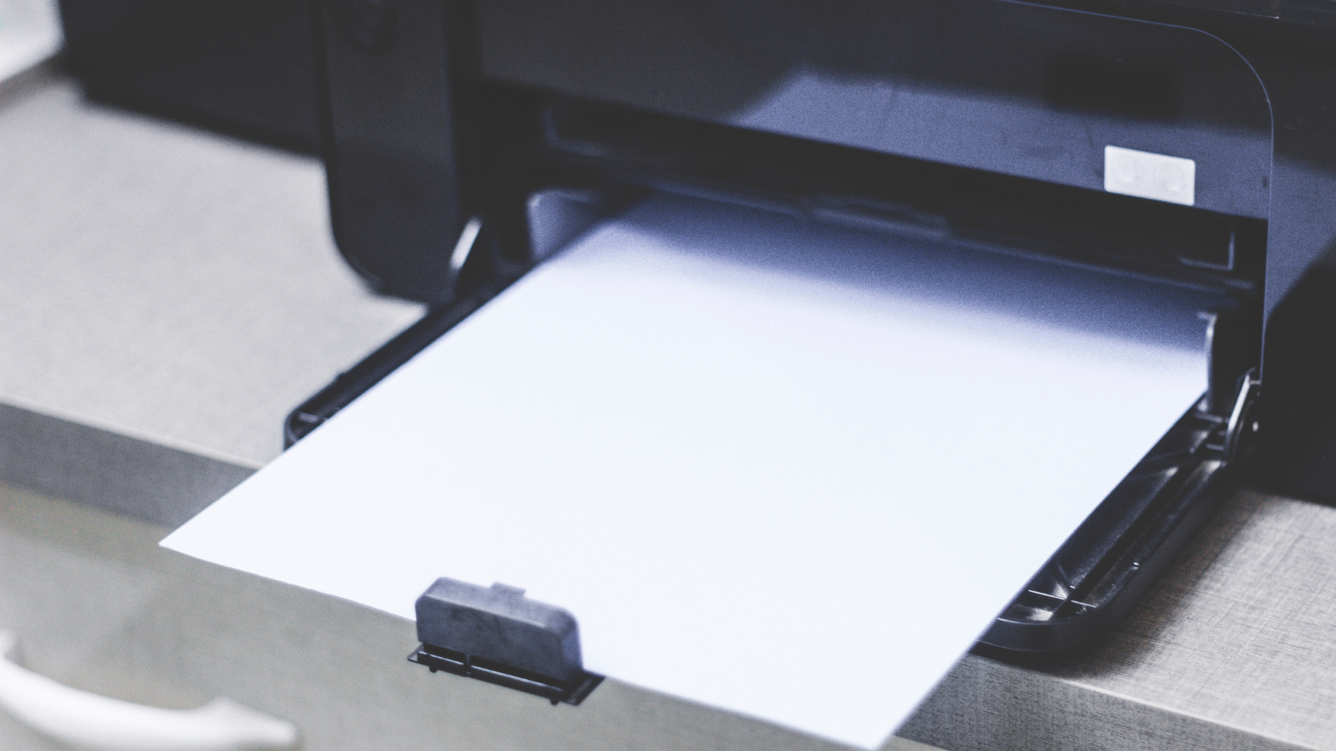 A black printer with a blank white paper in the output tray.