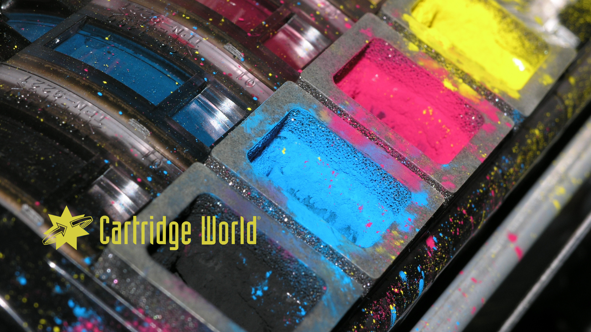 Close-up of ink cartridges filled with cyan, magenta, yellow, and black toner powder; logo for
