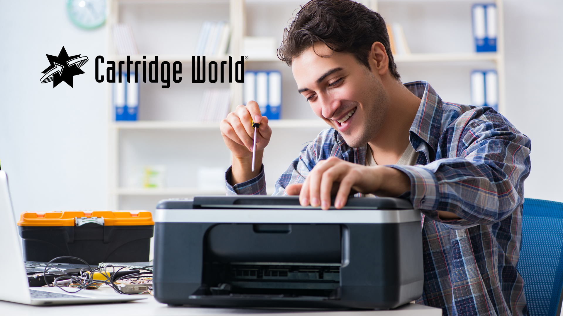 Man smiling while working on a printer, logo for Cartridge World in the background.
