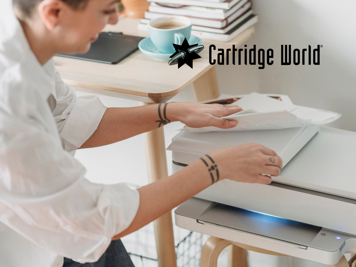 Woman loading paper into a printer at a desk, Cartridge World logo.