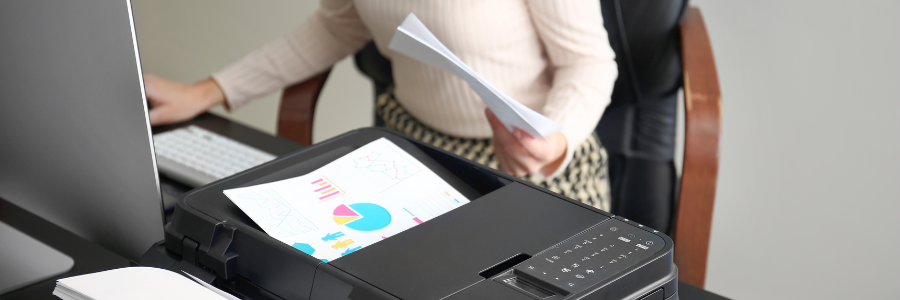 Person standing by a printer with a printed pie chart. They are holding papers and looking at the printer.