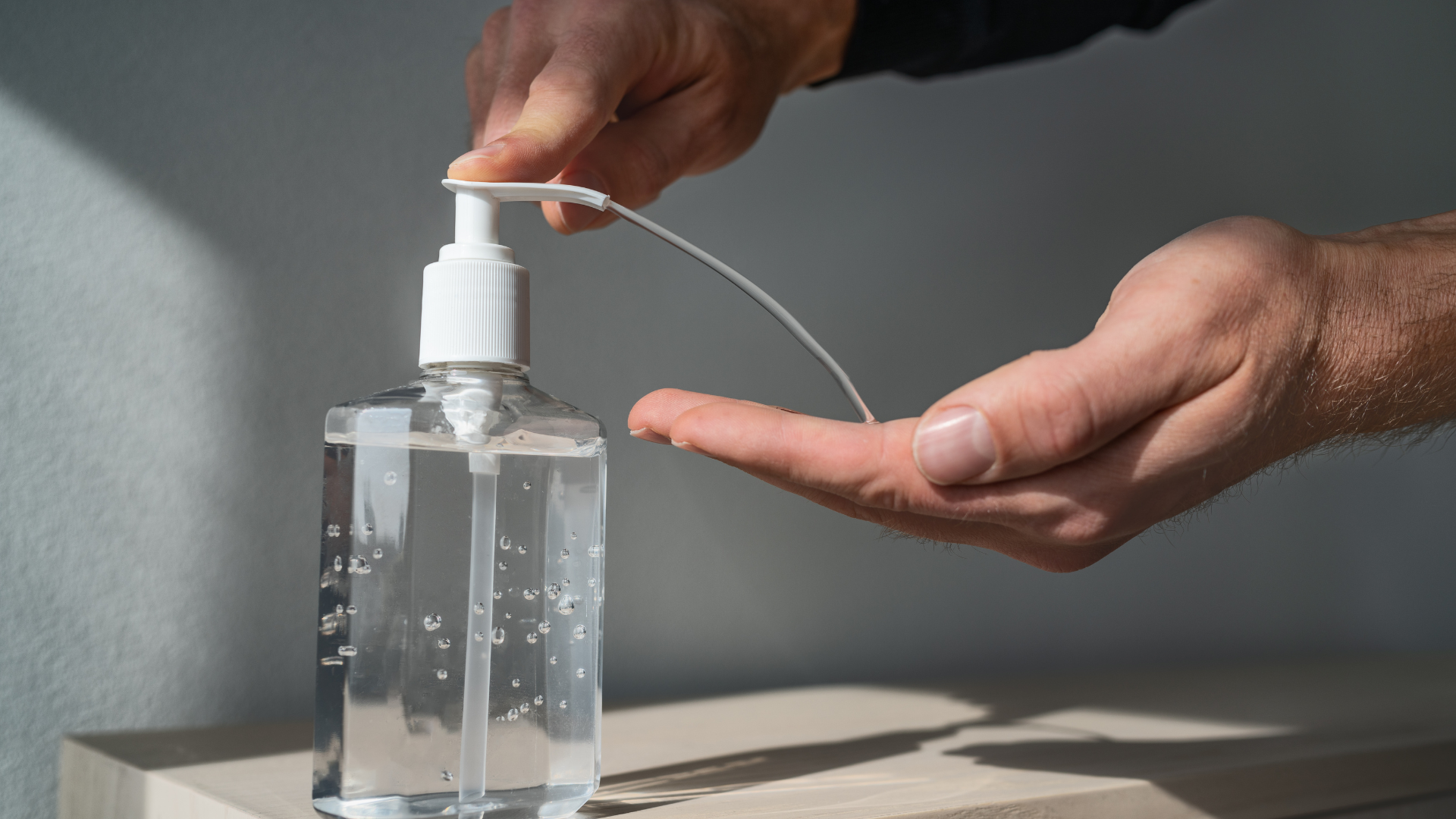 Person dispensing hand sanitizer from a clear bottle onto their palm.