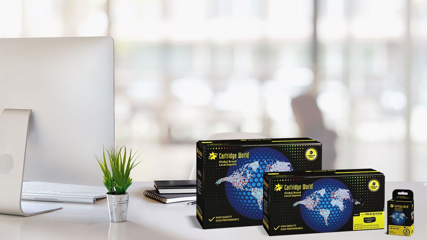 Boxes of product with a globe graphic on a desk with a computer and plant.