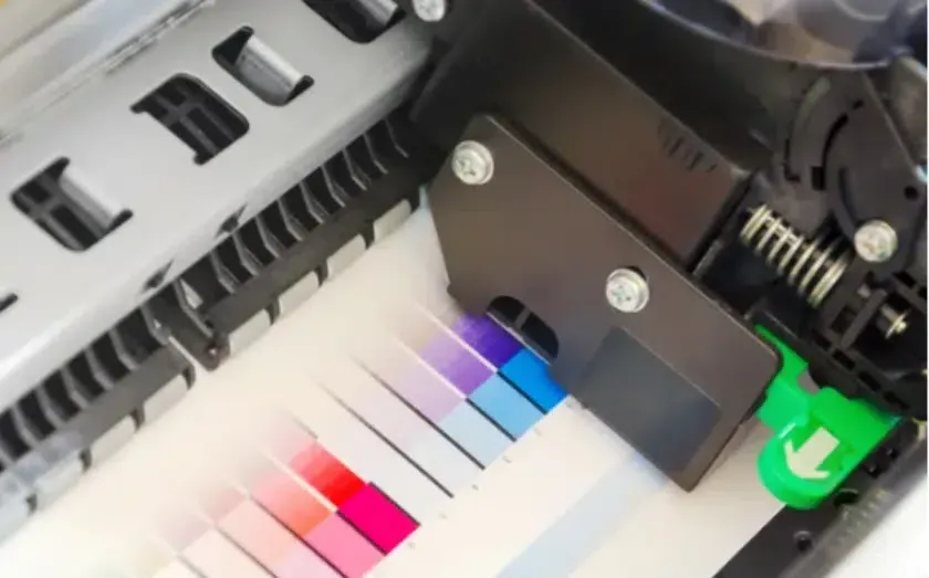 Close-up of a printer head printing color swatches on a white sheet of paper.