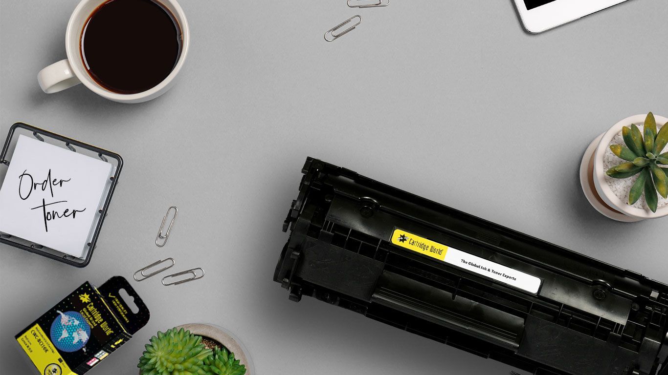 Office desk with coffee, toner cartridge, notepad, and small plants.