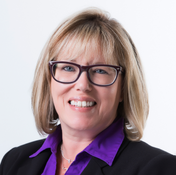 Woman with short blonde hair, wearing glasses and a purple shirt, smiling, business portrait.