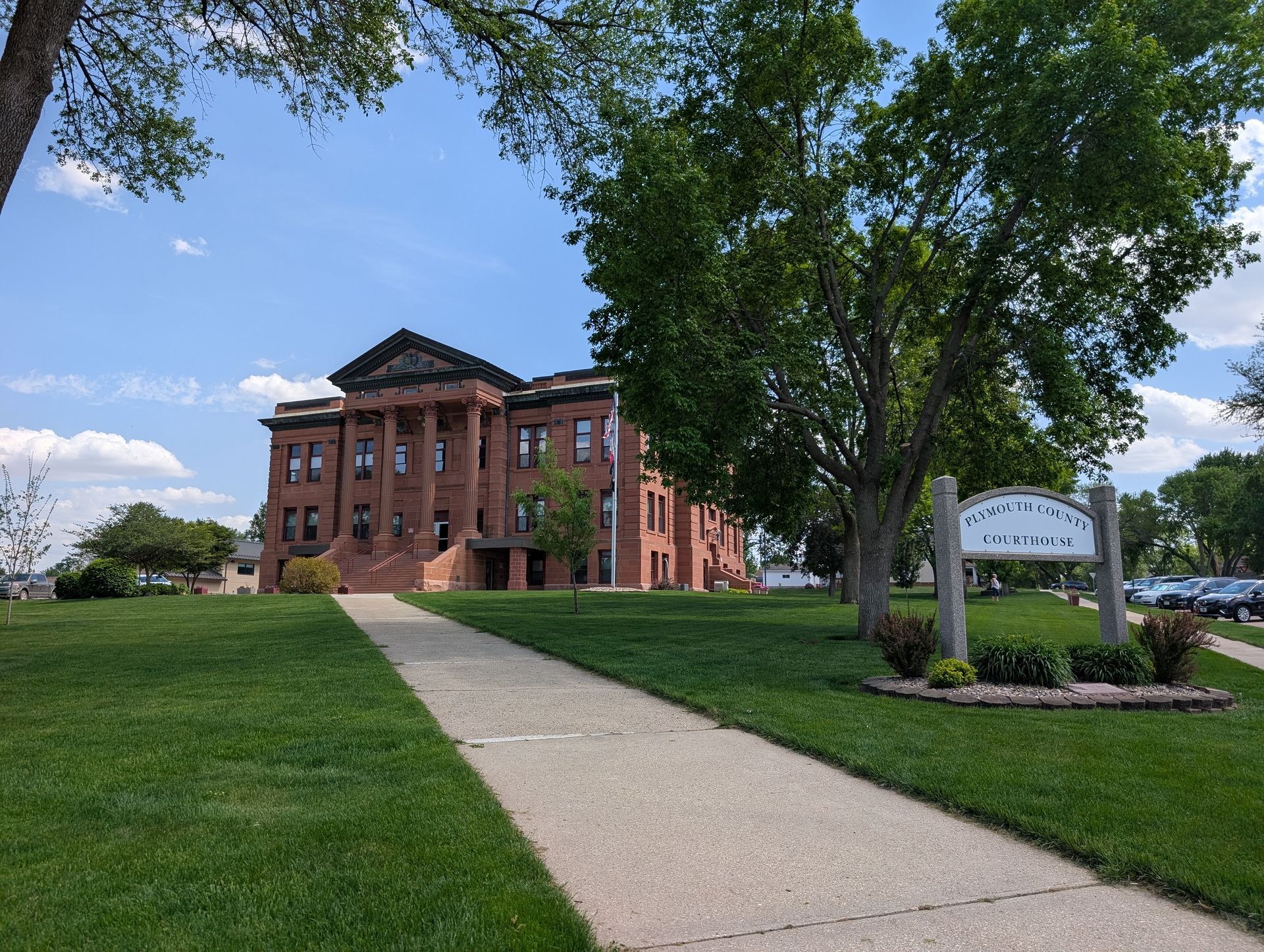 Brick academic building with columns beside a sidewalk and green lawn under a blue sky